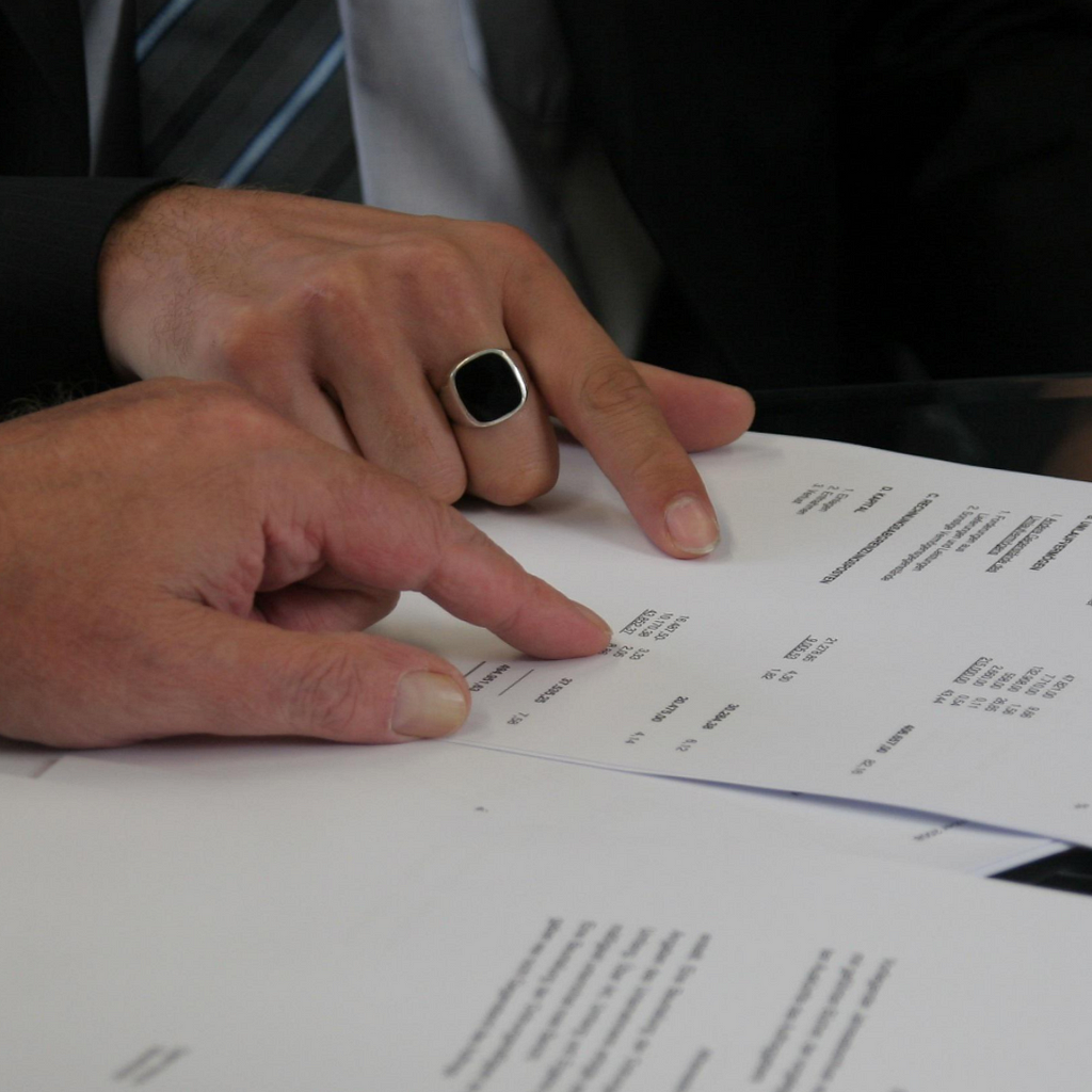 A close up of two seperate hands that are pointing to what appears to be a contract.