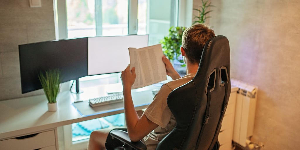 A modern-day teenage boy sitting at a desk with a computer and book.