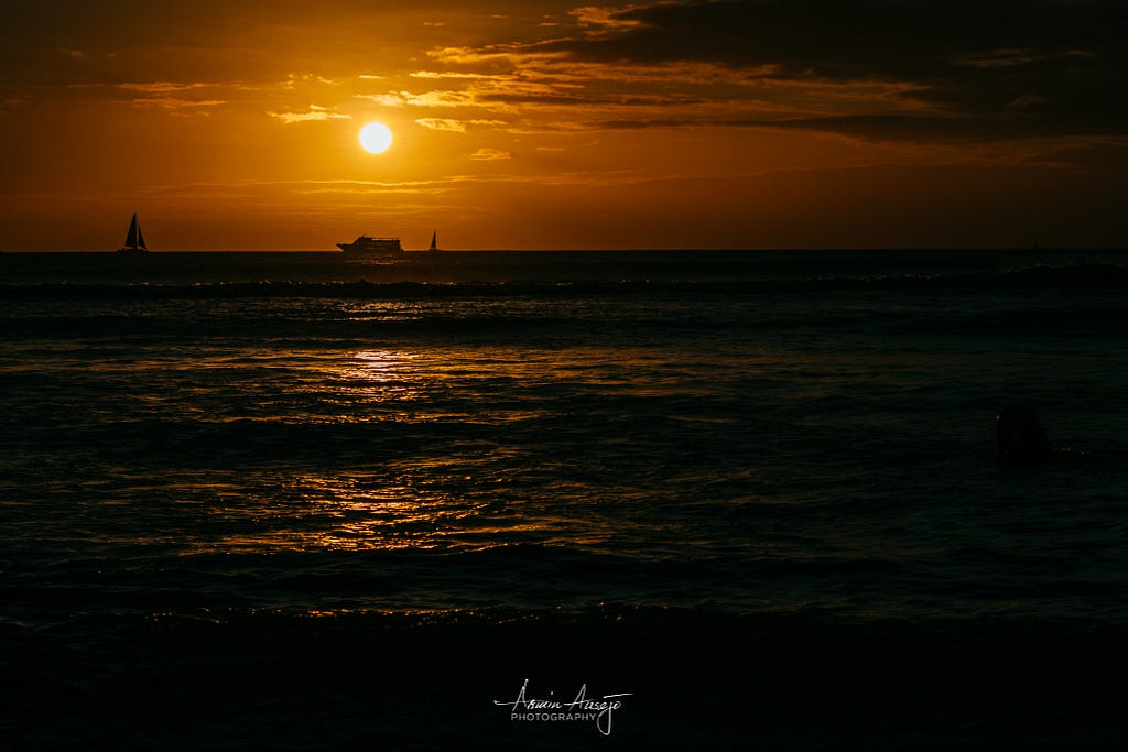 A cruise ship travels under the sun as it sets over Waikiki Beach