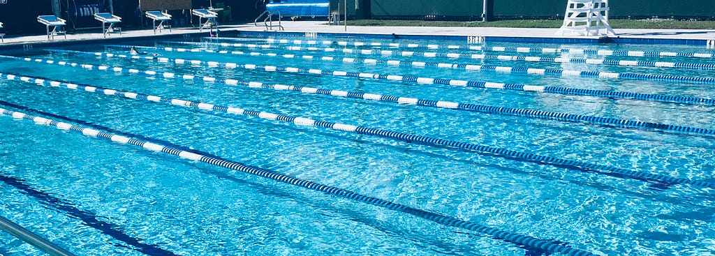 A color photograph of an 8 lane, 25 yard long swimming pool with aqua blue water and blue and white lane lines.