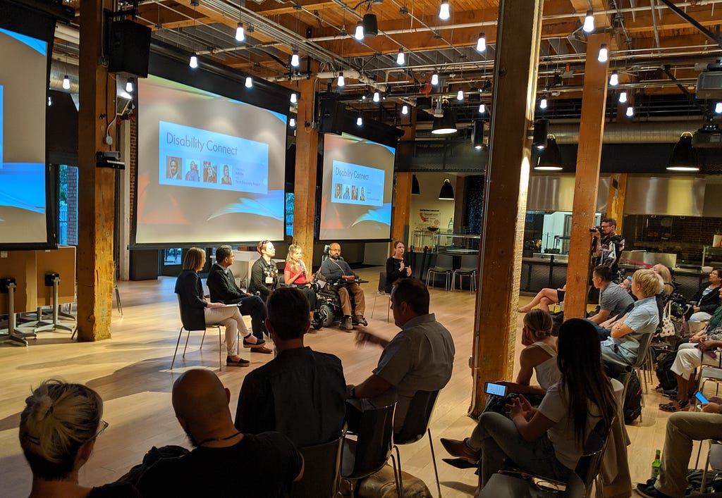 4 panelists, a moderator, and an ASL interpreter sit in front of an audience during Disability Connect at Adobe SF.