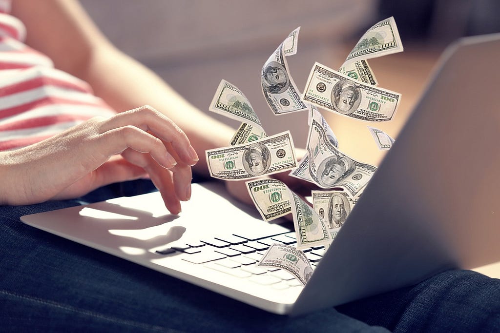 Woman typing on a laptop. Dollar bills are flying out of the laptop.