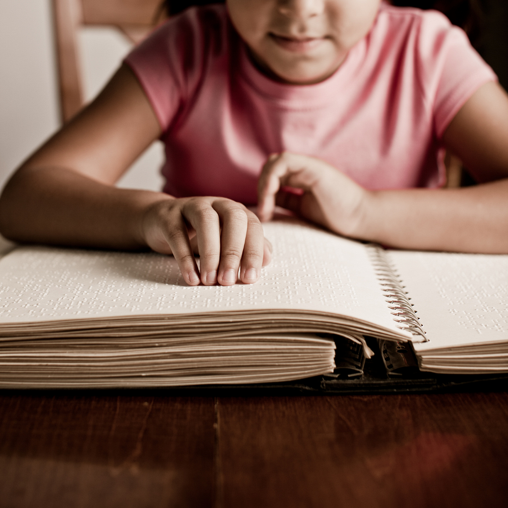 Niña con una camiseta rosada leyendo en Braille