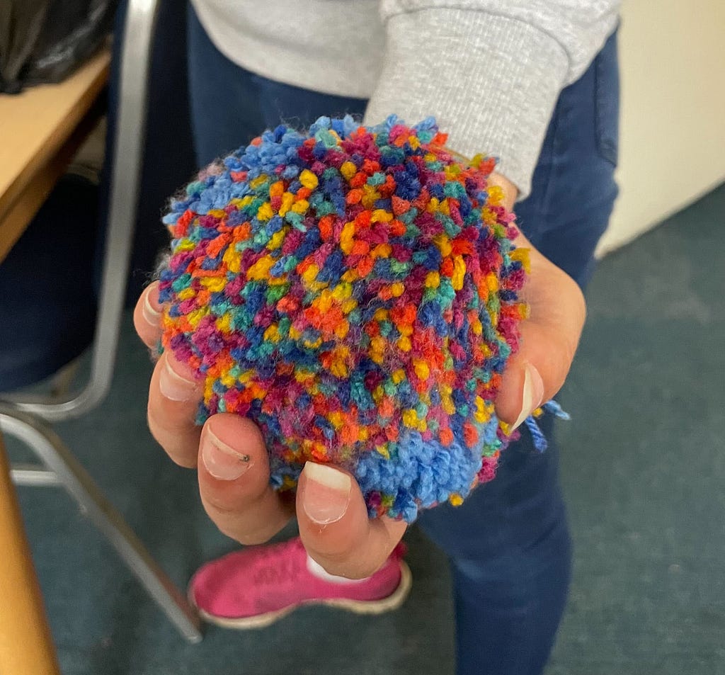 A hand holding a multicoloured pom-pom