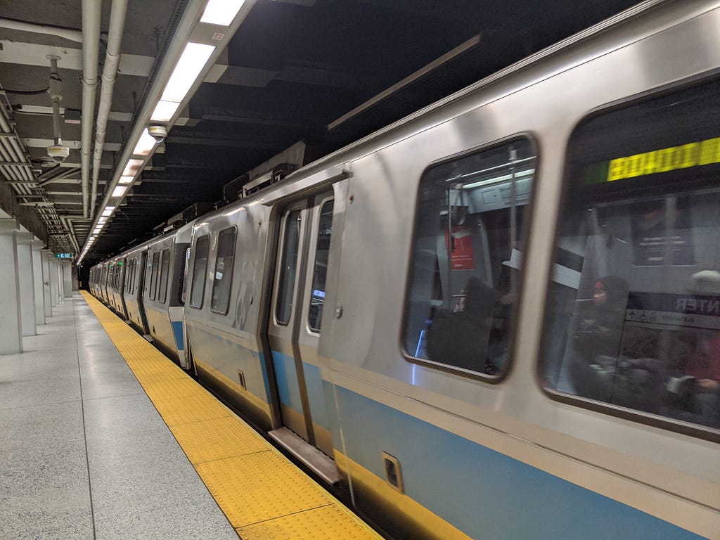 A MBTA blue line train dwelling at a station. No one is on the platform.