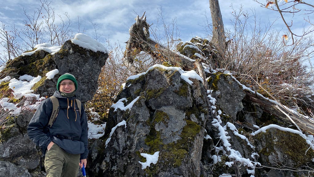 WWU Geology graduate student Brendan Garvey stands in front of a snow-dusted rock formation.