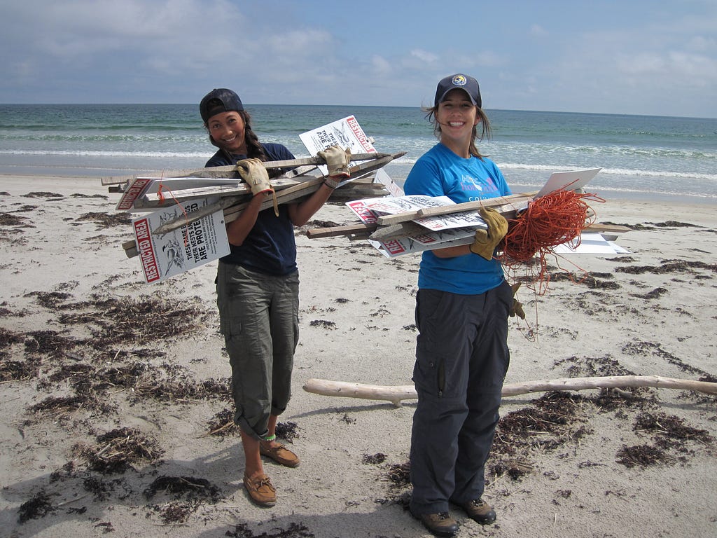 Two young ladies carrying a bundle of signs on the beach