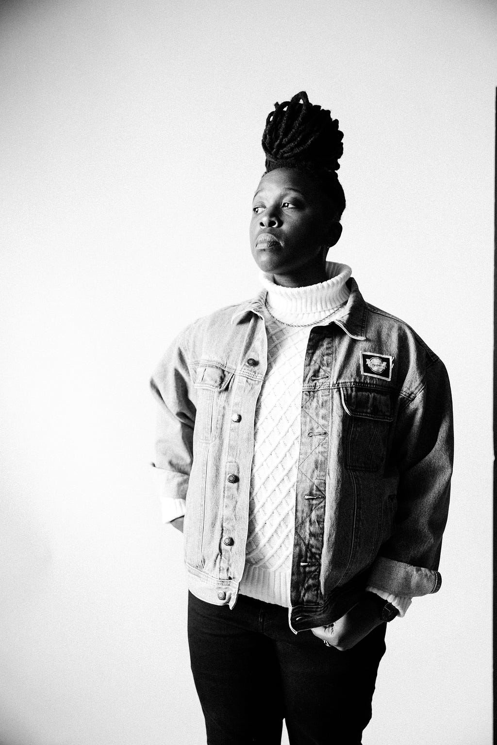 a black & white self-portrait of myself with my hair in a bun, wearing a white turtleneck, jean jacket while looking toward the light.