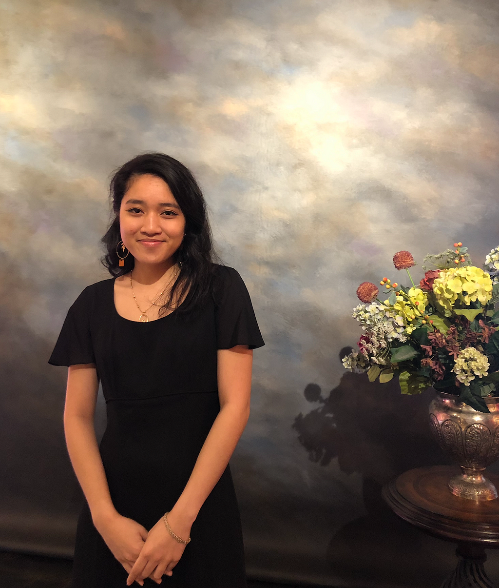 Thria Bernabe poses next to flowers indoors.