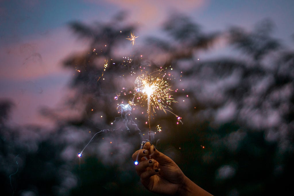 Anonymous woman showing burning sparkler against evening sky