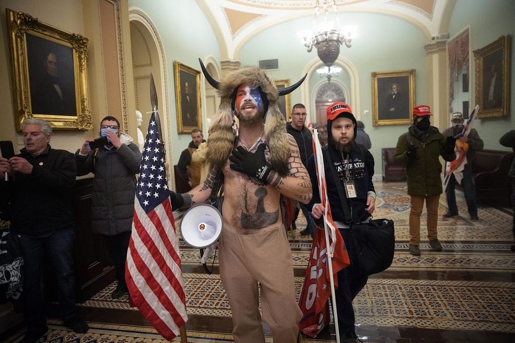 One of the most recognizable figures in the crowd was a man in his 30s with a painted face, fur hat and a helmet with horns. The protester, Jacob Chansley — known by followers as the QAnon Shaman — quickly became a symbol of the bizarre and frightening spectacle.