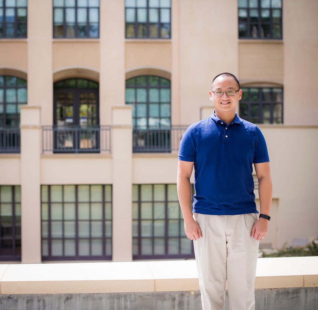 A person (Henry Ngo) wearing a navy polo and khaki slacks; in the background is the Sherman Fairchild Library at the California Institute of Technology