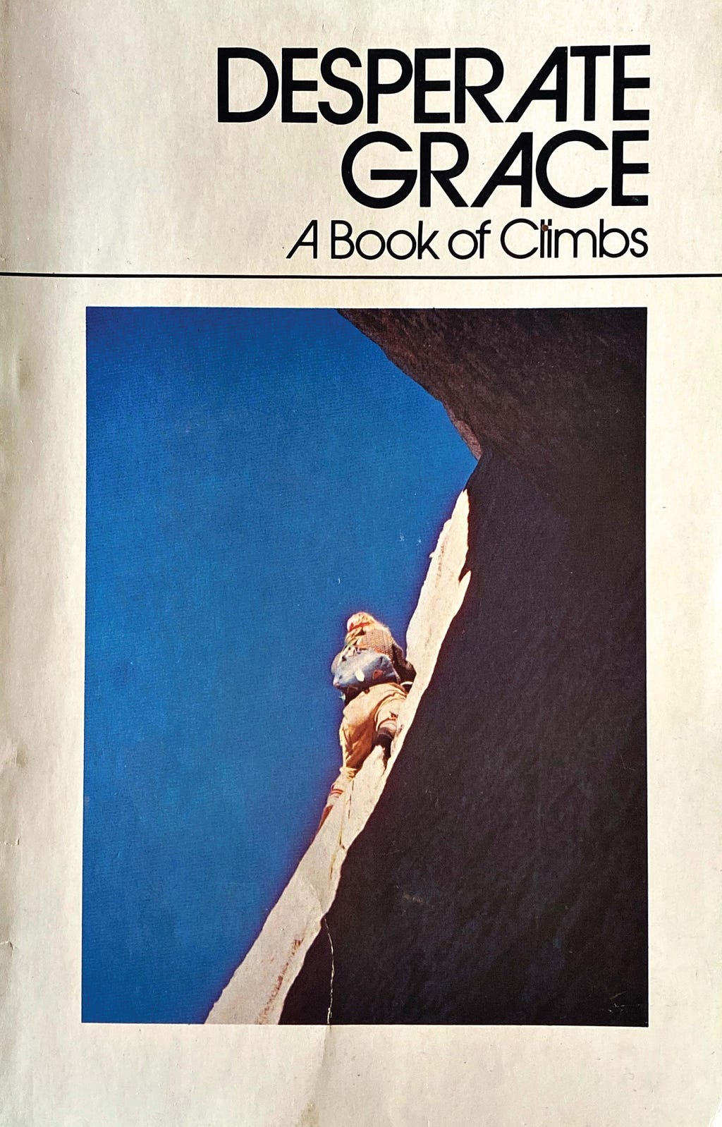 A photograph of the cover of an older book, with the title “DESPERATE GRACE: A BOOK OF CLIMBS” visible above a photograph of a person climbing up a rock wall.