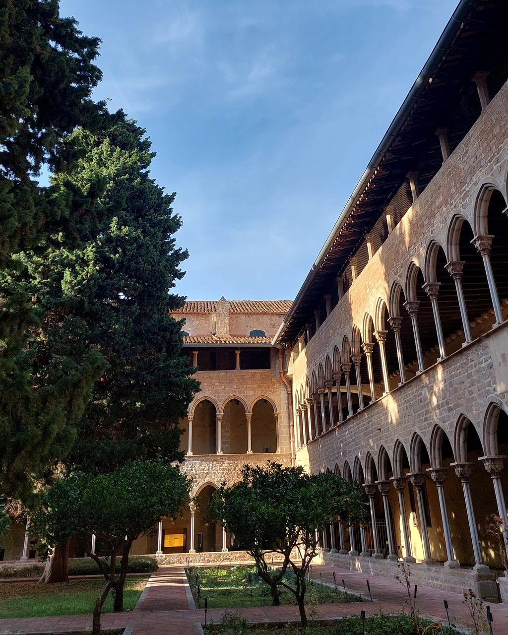 Image of the arches of the Pedralbes Monastery, with a blue sky on the top and a garden in front.