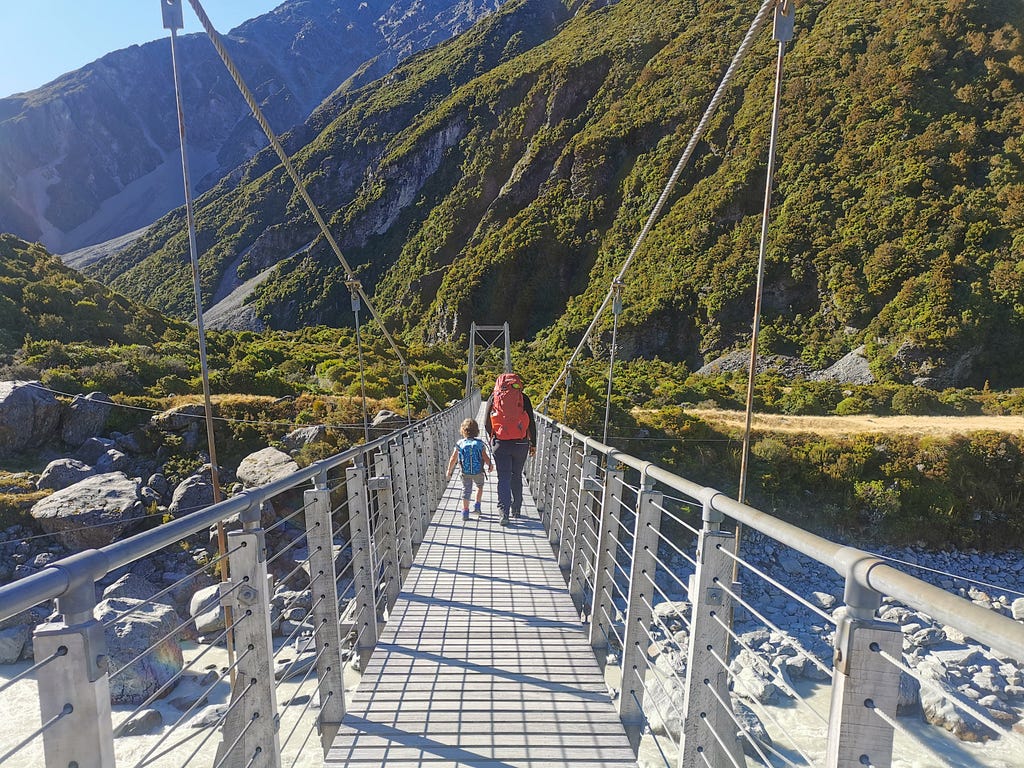 A dad and son walk across a swing bridge.