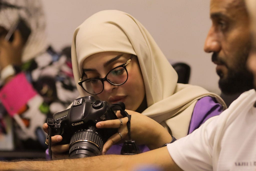 A woman wearing hijab looks into the view screen of the camera she is holding.
