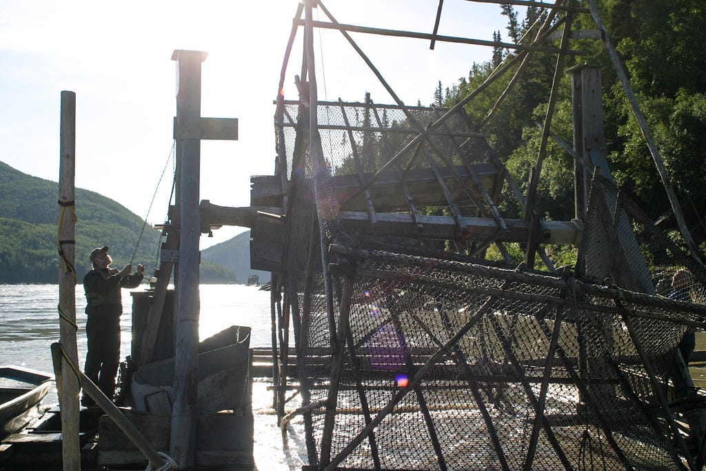 a man standing next to a large fish wheel in a river