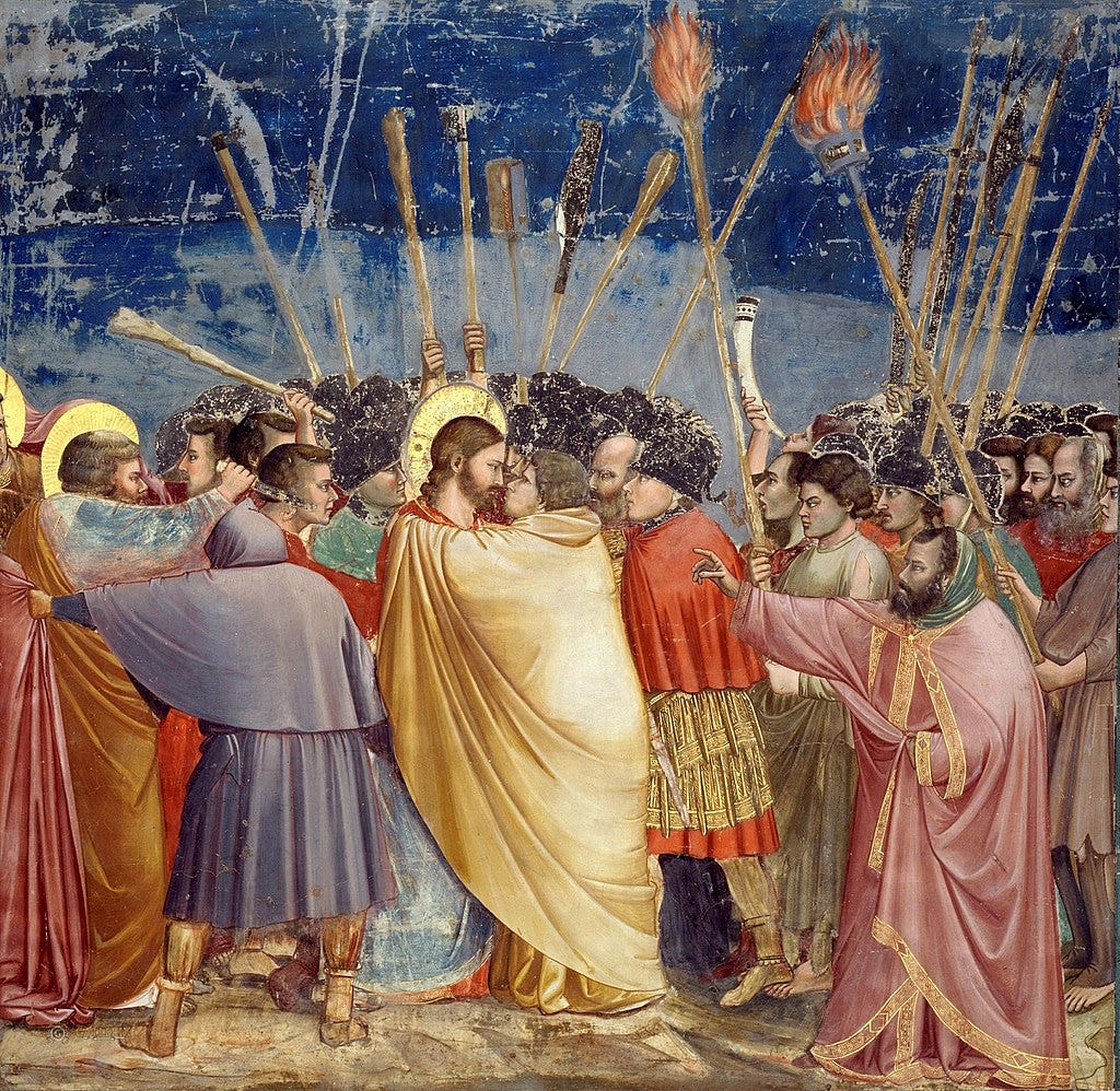 Fresco painting by Giotto di Bondone titled The Kiss of Judas, depicting the moment Judas betrays Jesus with a kiss. Jesus, haloed and calm, meets Judas’ gaze as the two stand at the center of a chaotic crowd. Soldiers and onlookers press in, brandishing torches and clubs. The composition is dense with movement, tension, and expressive faces, capturing both the intimacy and violence of the scene. Painted in the early 14th century in the Scrovegni Chapel, Padua.