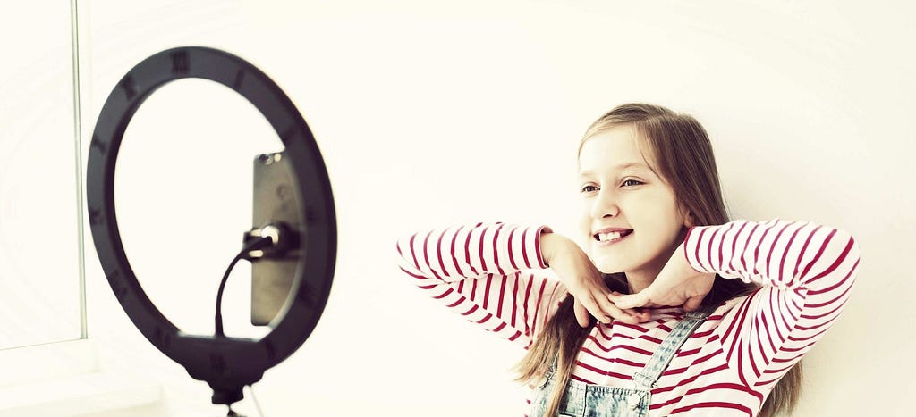 Young girl posing in front of a ring light and a mobile phone