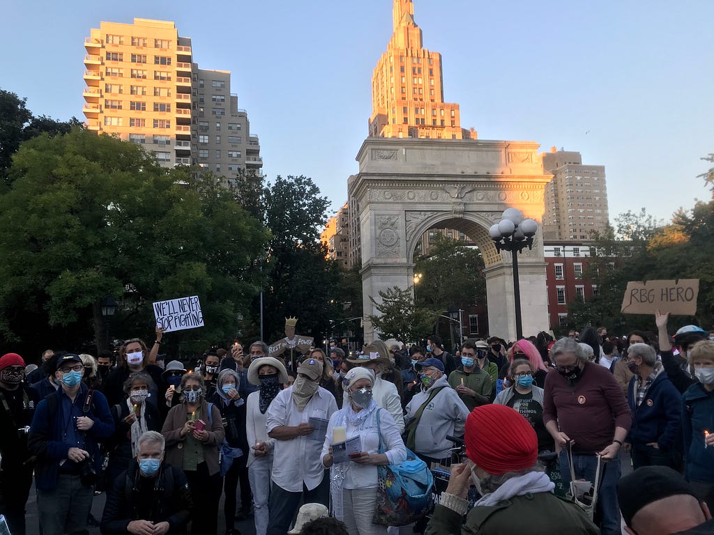 A large group of mourners gathered together with some holding signs referencing Ruth Bader Ginsburg