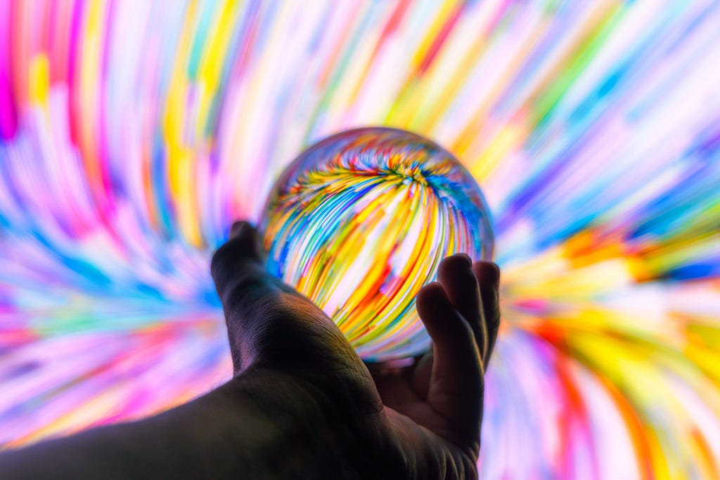 a hand holding a glass ball with multi-colored streaks in front of a multicolored streak background