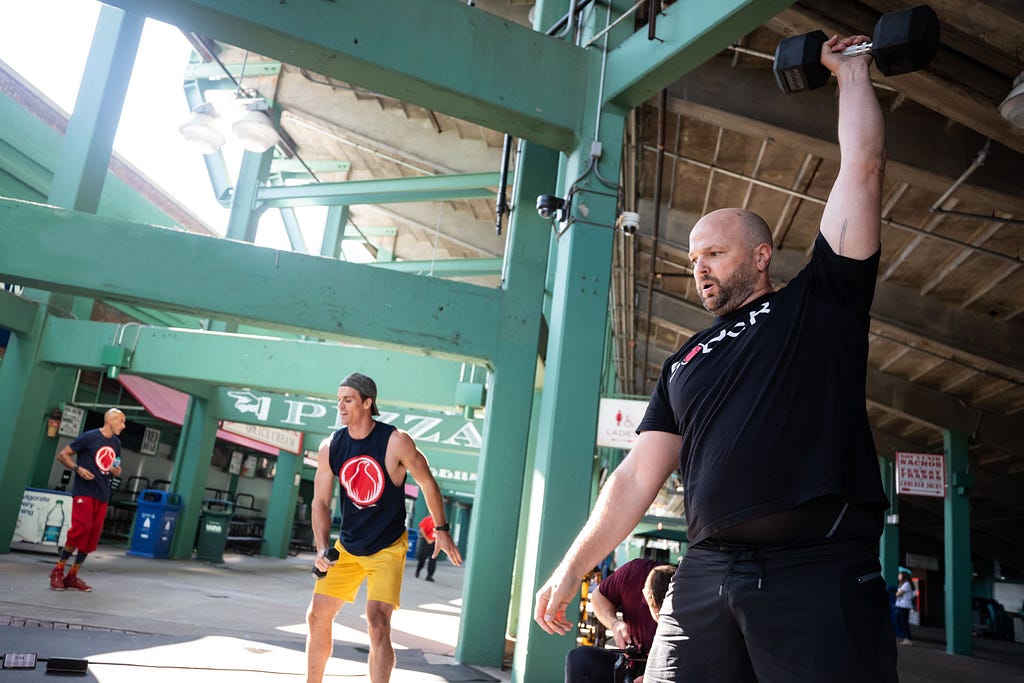 Scott Strode lifting a weight in the foreground on the right, while another person is exercising in the background in the middle of the picture.