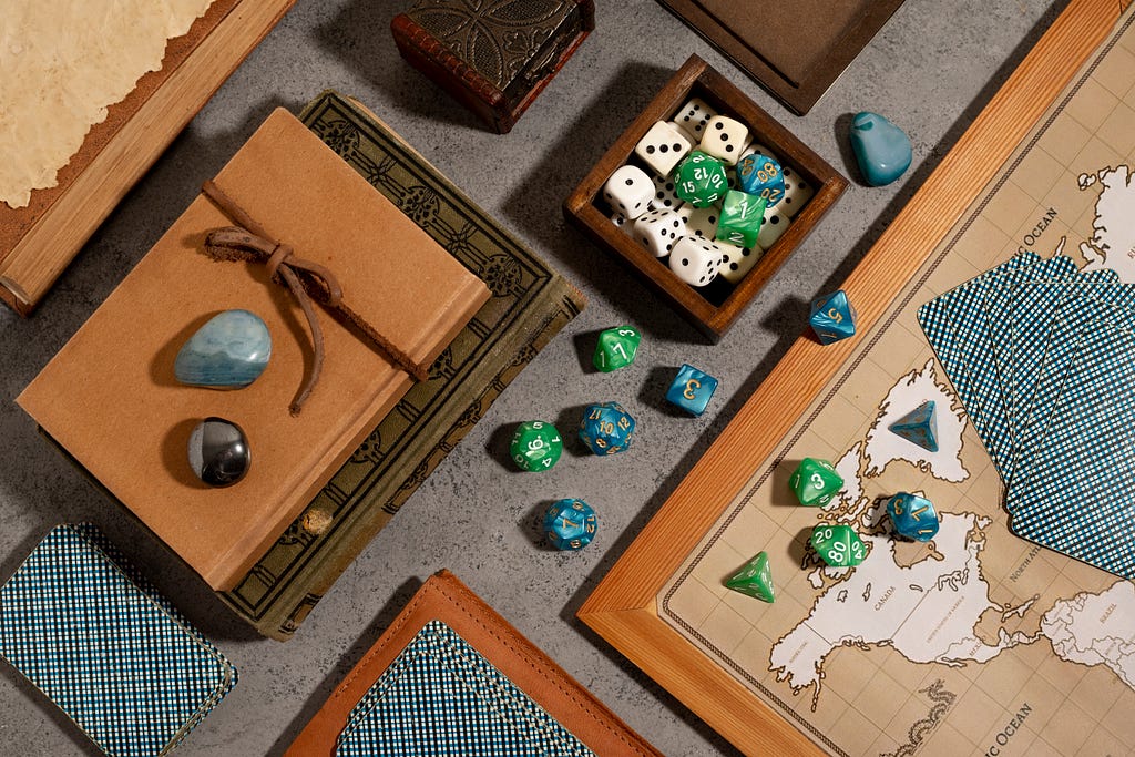 An unknown board game on the table. There are dice of different shapes, playing cards, bound books, and a leather journal on the table, arranged aesthetically.