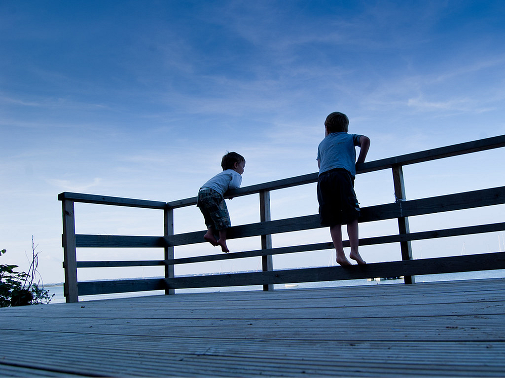 Two boys playing on a wooden fence.
