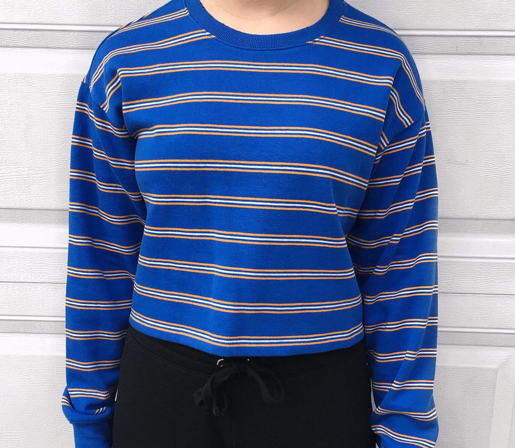 A blue sweater with white and yellow stripes. Worn with black joggers.