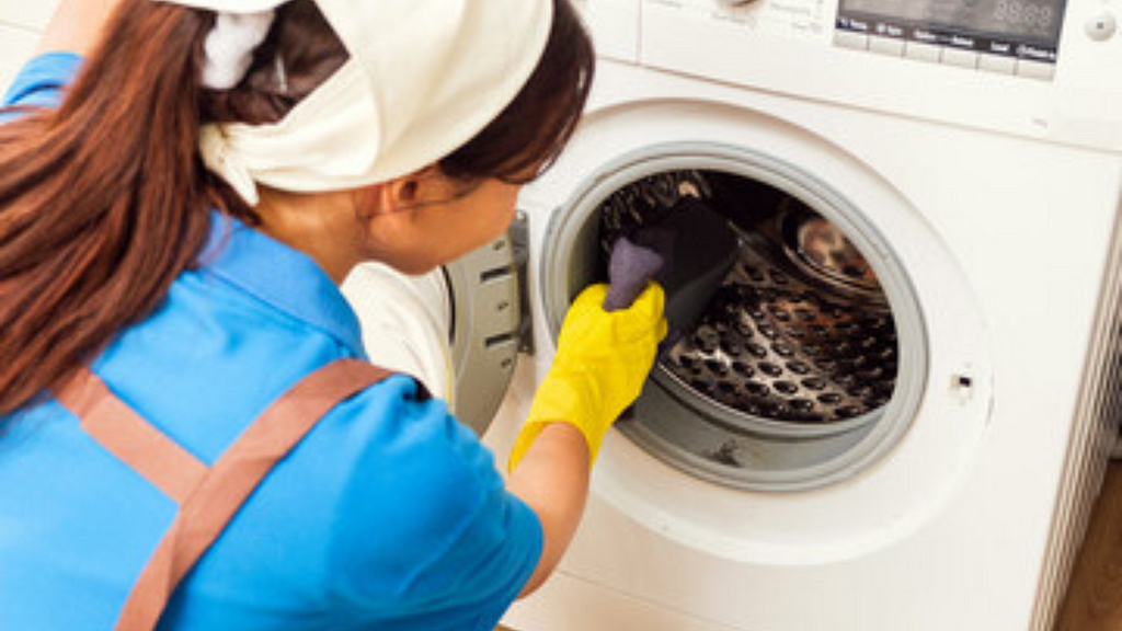 Image showing a girl with blue top scrubbing the inside of a washing machine drum with a sponge and cleaning solution.