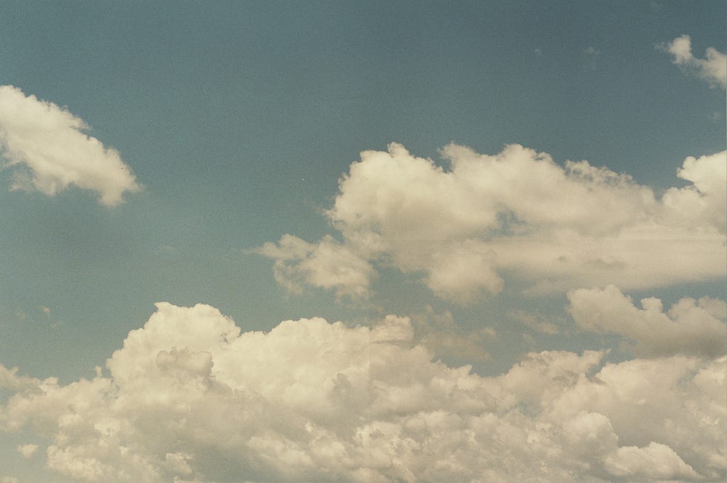 A hazy film photograph of a cloudy blue sky.