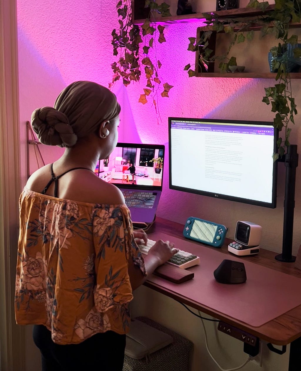 Black woman working on a computer at a standing desk, with purple lights.