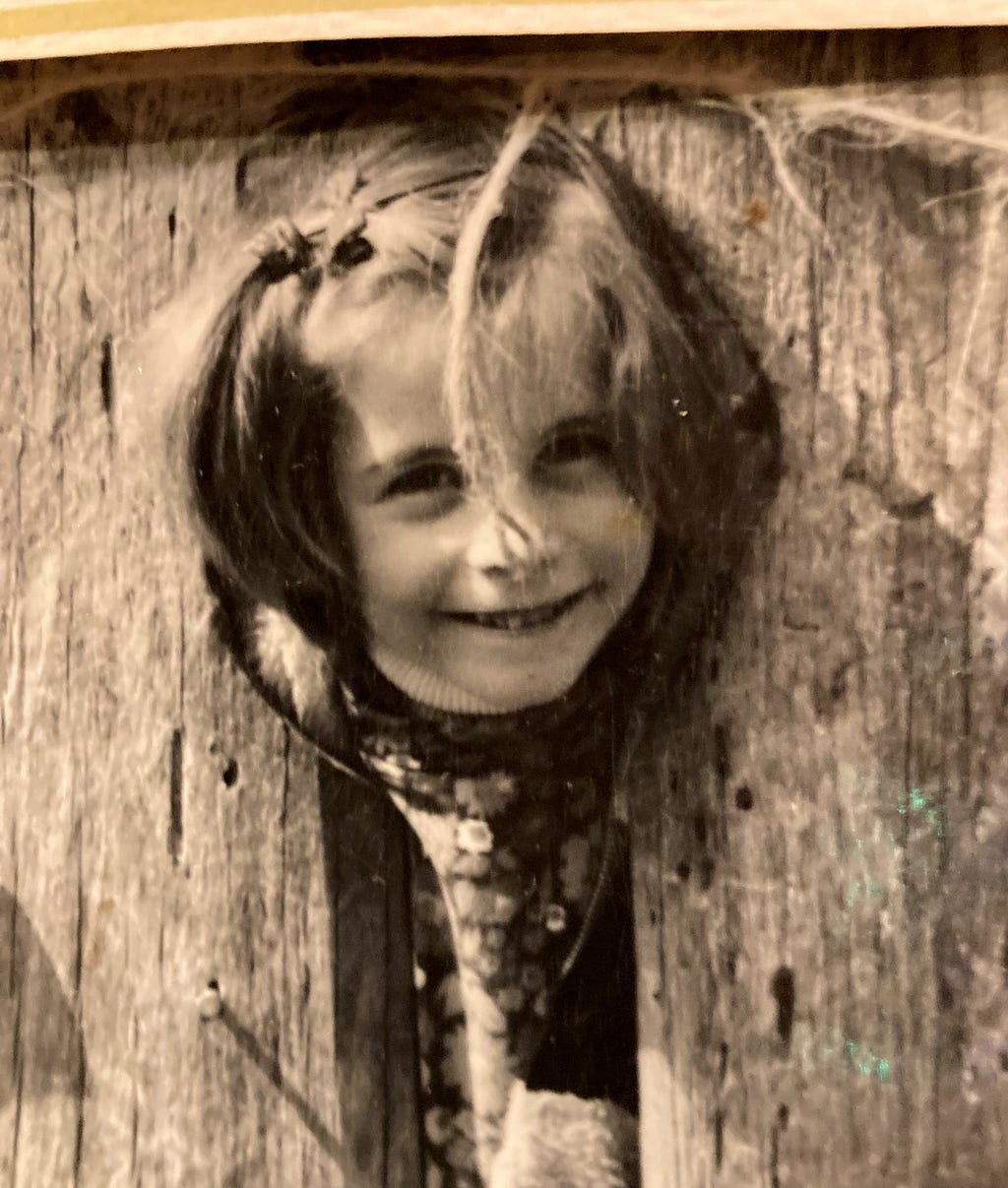 A young girl in an aged photograph sticks her head out between two pieces of wood