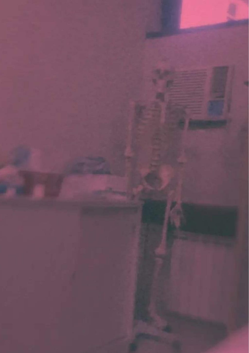 Fotografía en tonos rojizos y efecto borroso de un esqueleto de muestra en un consultorio médico.