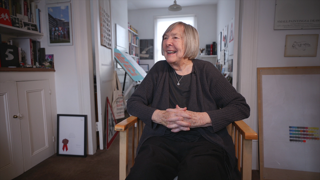 Margaret Calvert seated and smiling in her London studio