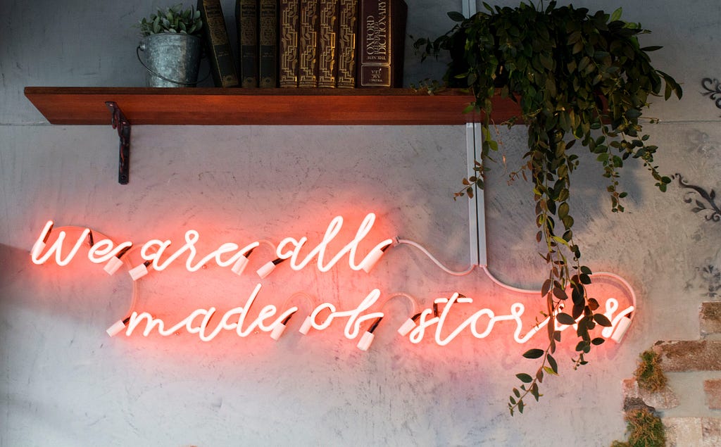 A neon sign reads “We are all made of stories”