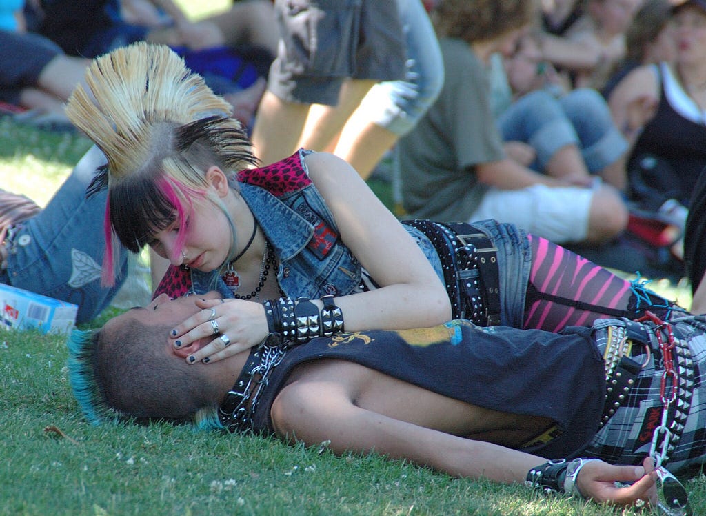 Two punks in love, on the grass in a crowd. Seemingly in a park