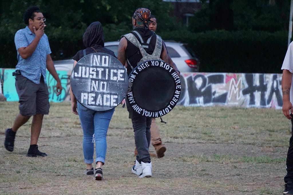 Two people walk away from the camera with round shields on their backs