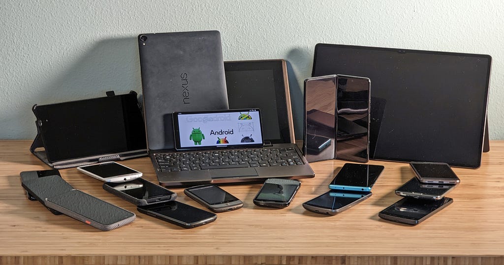 A table covered by almost 20 Android devices of different shapes and sizes.