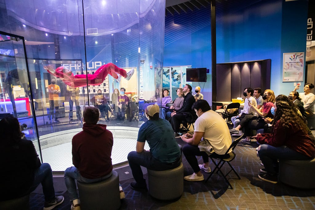 Students sitting around an air tunnel and watching an indoor skydiver take flight.
