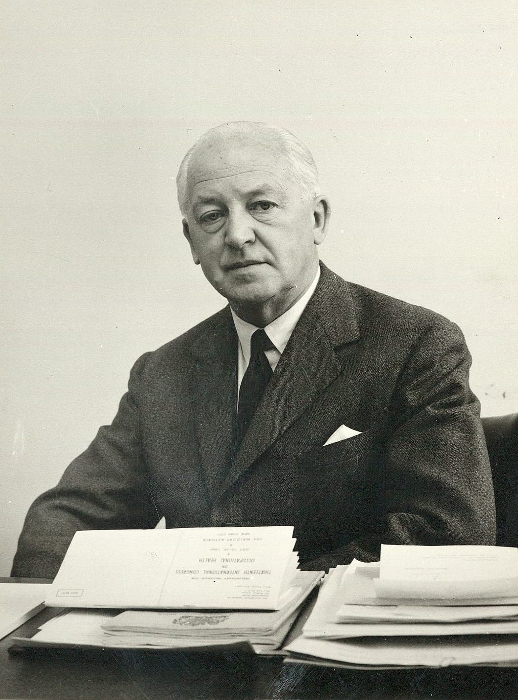 Black-and-white photograph of Ronald Lane, seated, with papers spread out on the desk in front of him