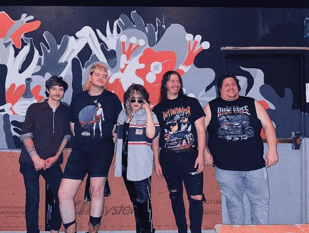 Ally and the band pose in front of a mural at The Loud