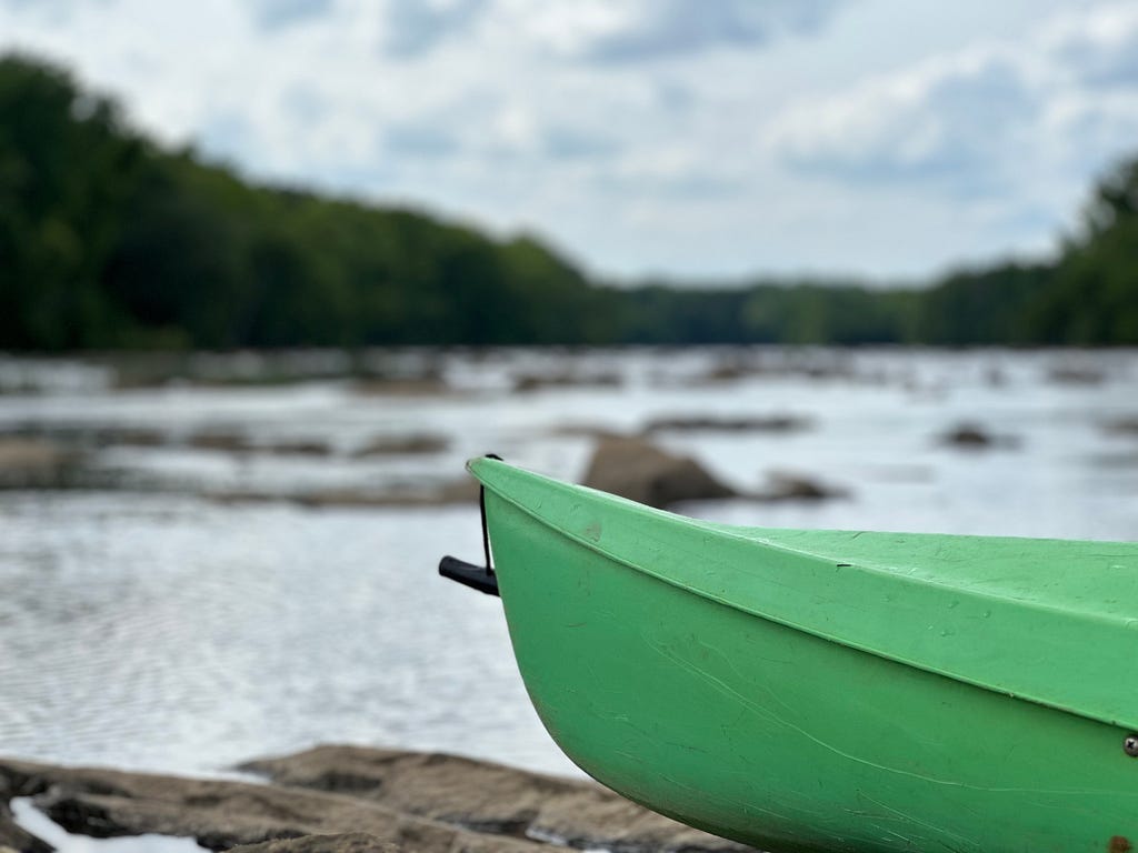 Bow of a green kayak on a rock with river and rocks in the background