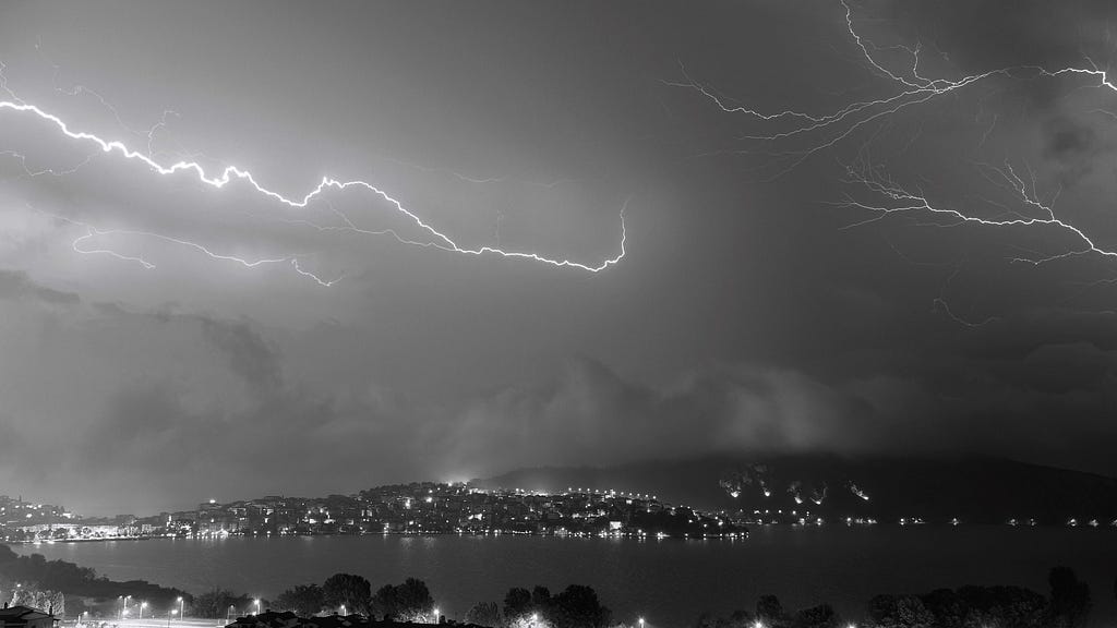 A black and white picture of lighting in the sky, over a bay city