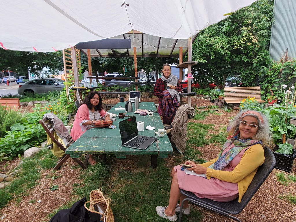 An outdoor image of three people — Tzunki, Laya and Llushan—gathered around a long table at the coFood Collaborative garden, with computers, underneath a white shelter.