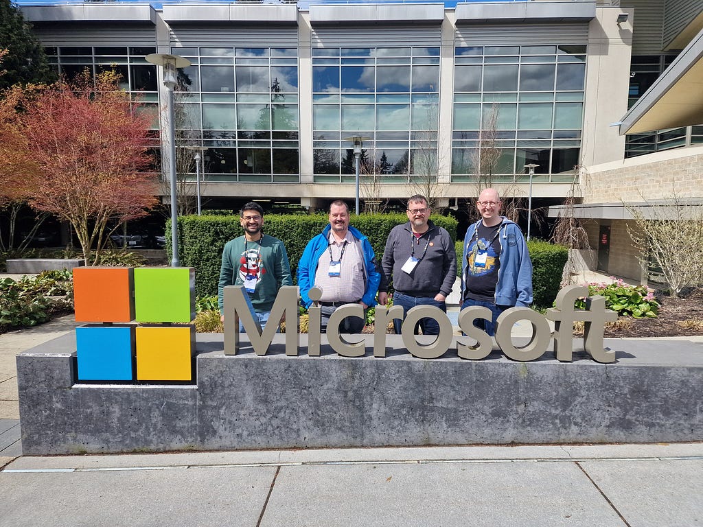 The Microsoft logo sign outside of Microsoft HQ in Seattle with Deepak Agarwal, Mike Hartley, Carl Cookson, Matt Collins-Jones all stood behind it smiling in the sunshine