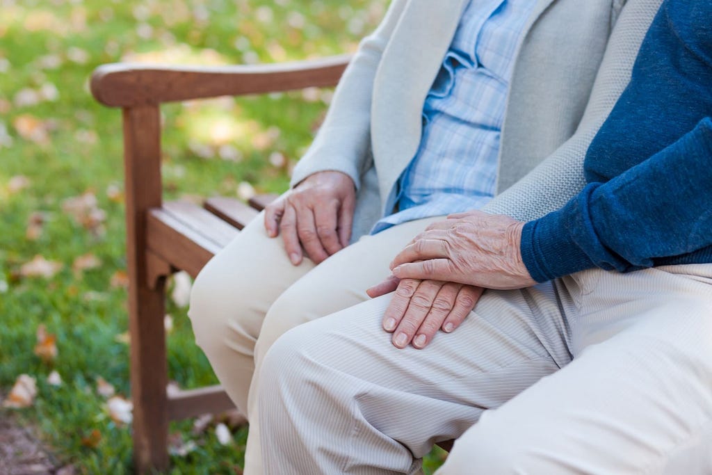 Eldre par sitter på benk og holder hender