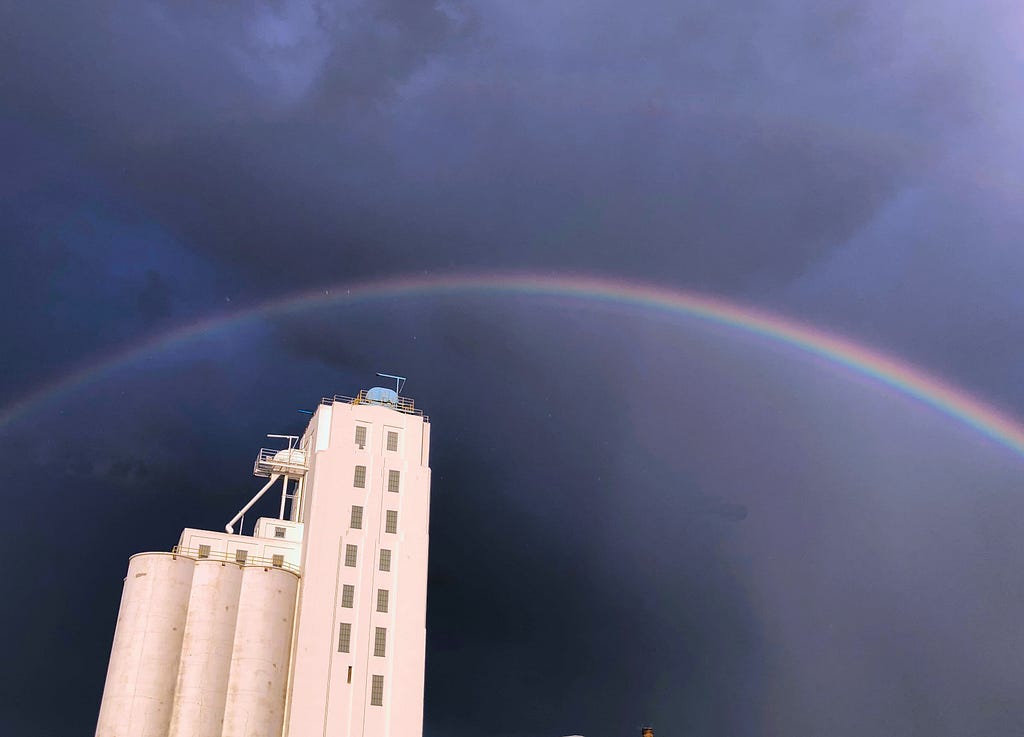 Rainbow over an industrial mill in a darkened, stormy sky.