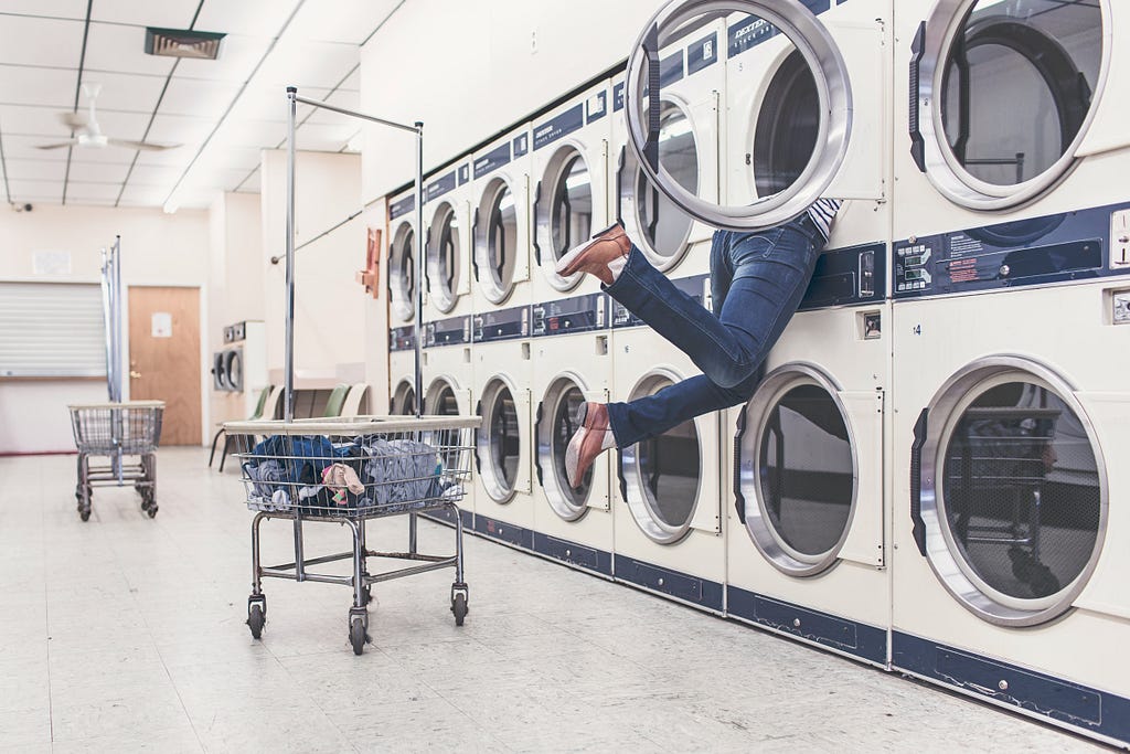 A person stuck in a washing machine, legs dangling out comically.