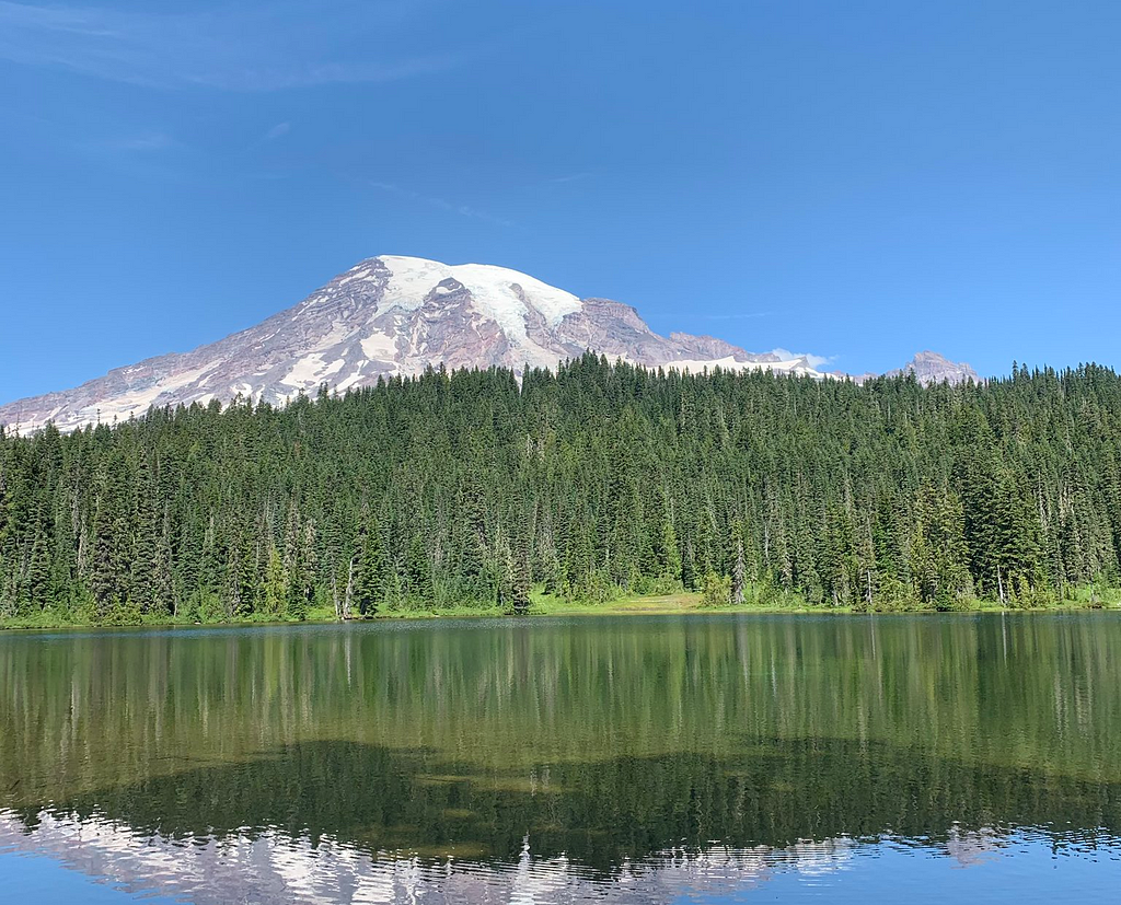 Mountain peeking over a tree line and reflecting on a lake